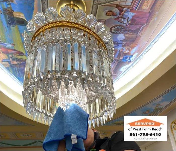 A cleaning technician carefully cleans a chandelier by hand. 