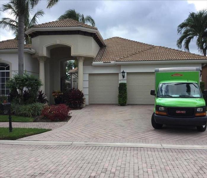 House with green SERVPRO truck parked in driveway.