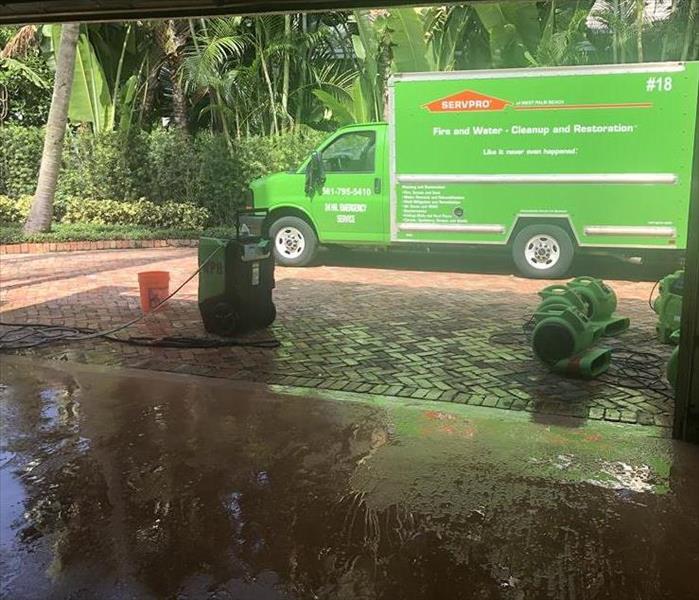 Garage with wet floor and SERVPRO green truck outside.